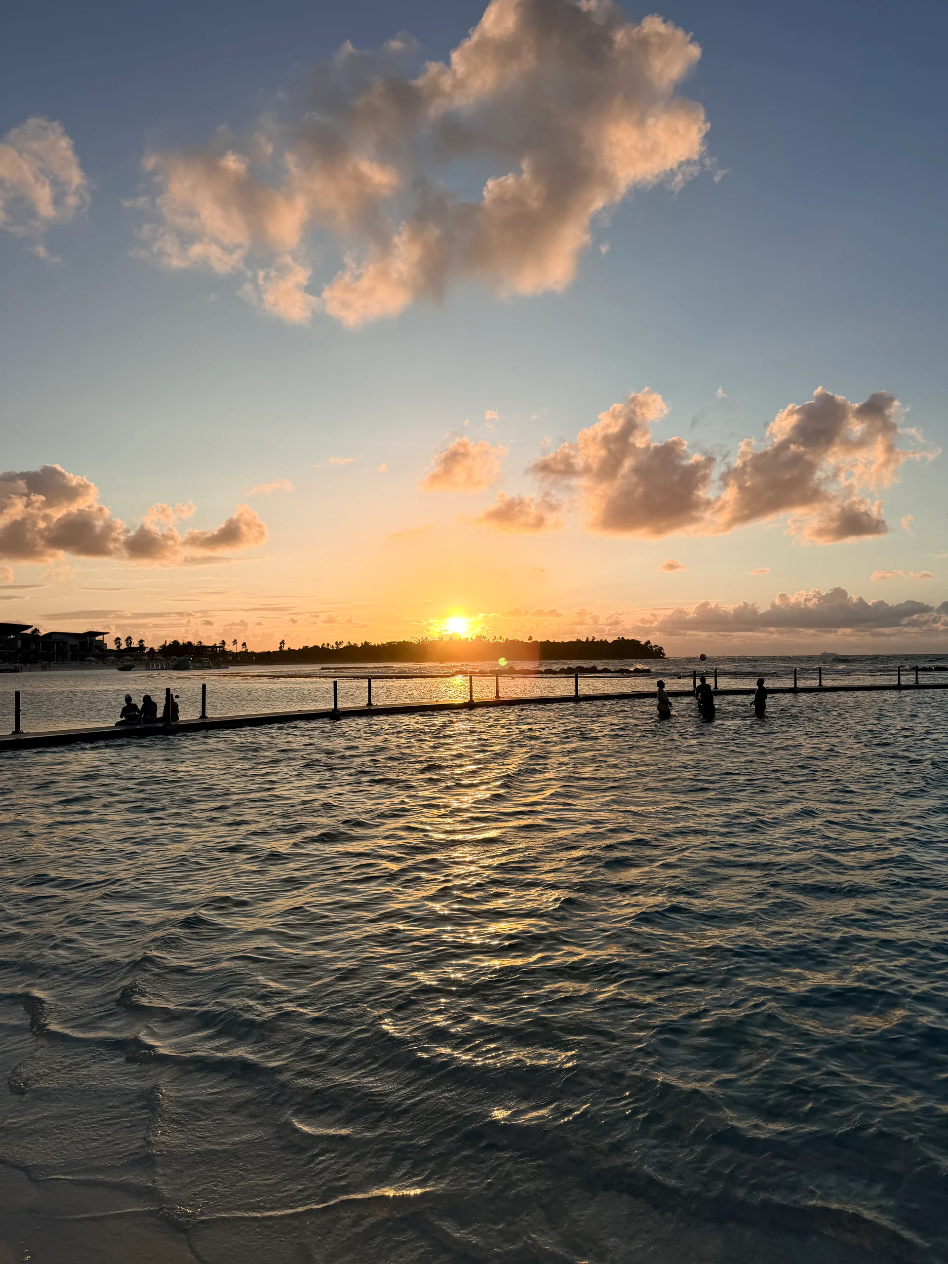 Un coucher de soleil serein au-dessus d'une piscine au Playa Escondida Resort au Panama. Les silhouettes de personnes nagent et se détendent tandis que la lumière dorée se reflète sur l'eau, créant une scène tranquille et pittoresque.