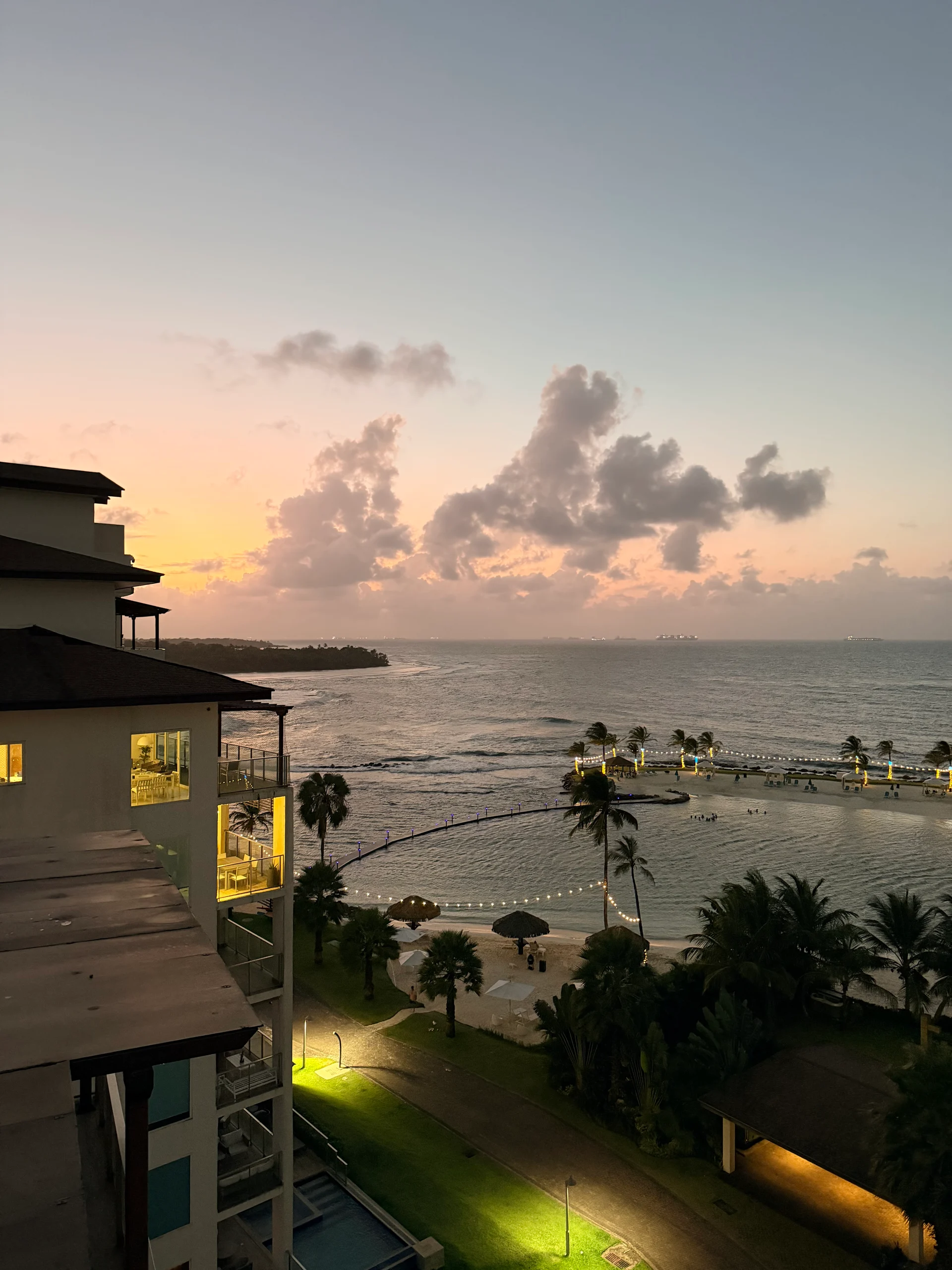 Vue imprenable du crépuscule du complexe Playa Escondida au Panama, mettant en valeur des bâtiments illuminés, une plage tranquille et un ciel de coucher de soleil vibrant. Les palmiers et les guirlandes lumineuses ajoutent à l'ambiance tropicale.