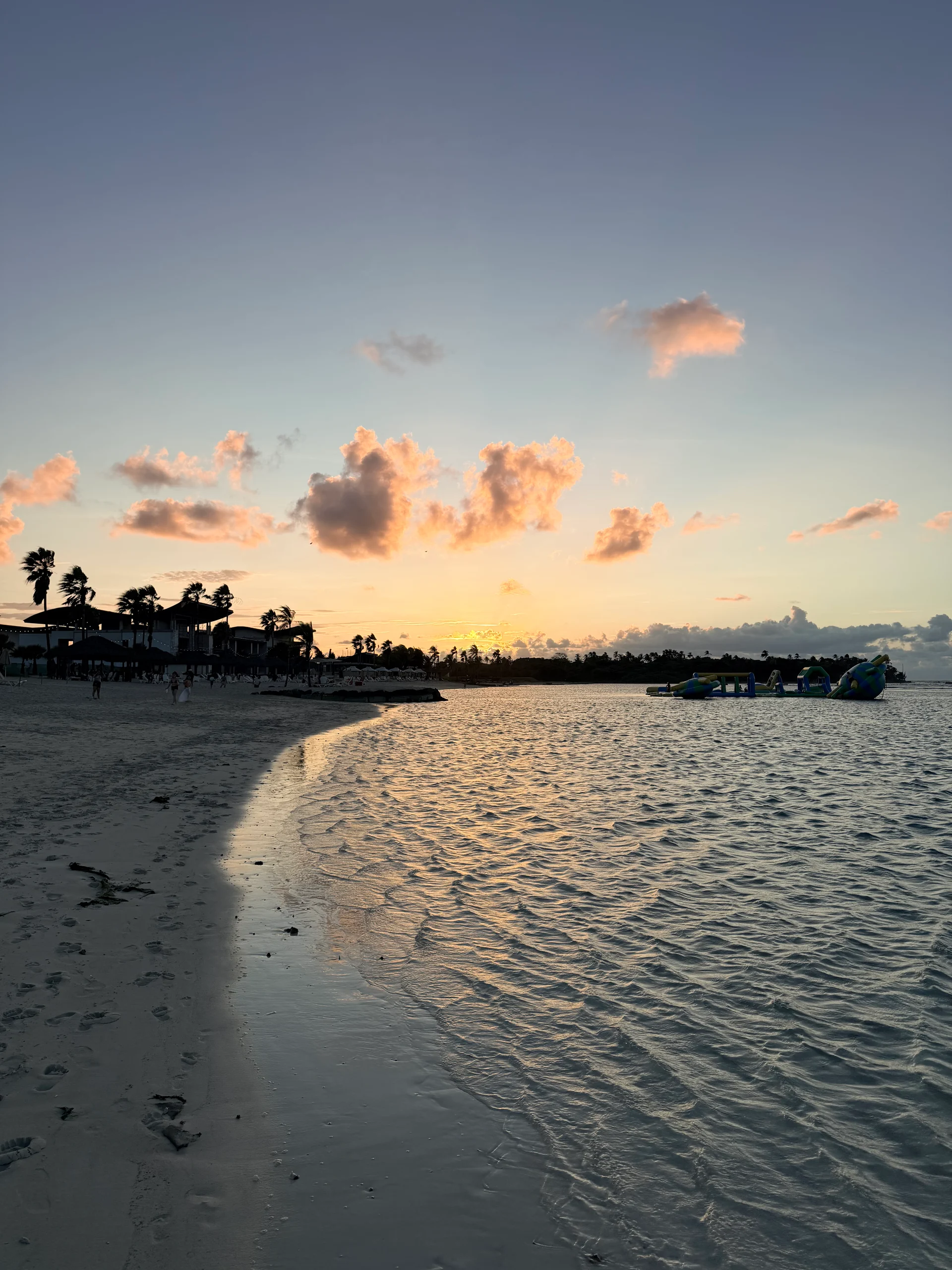 Une vue pittoresque du coucher de soleil sur les eaux turquoise tranquilles de Playa Escondida au Panama. Des palmiers en silhouette et des structures sur la plage encadrent la scène, créant une atmosphère sereine et accueillante.