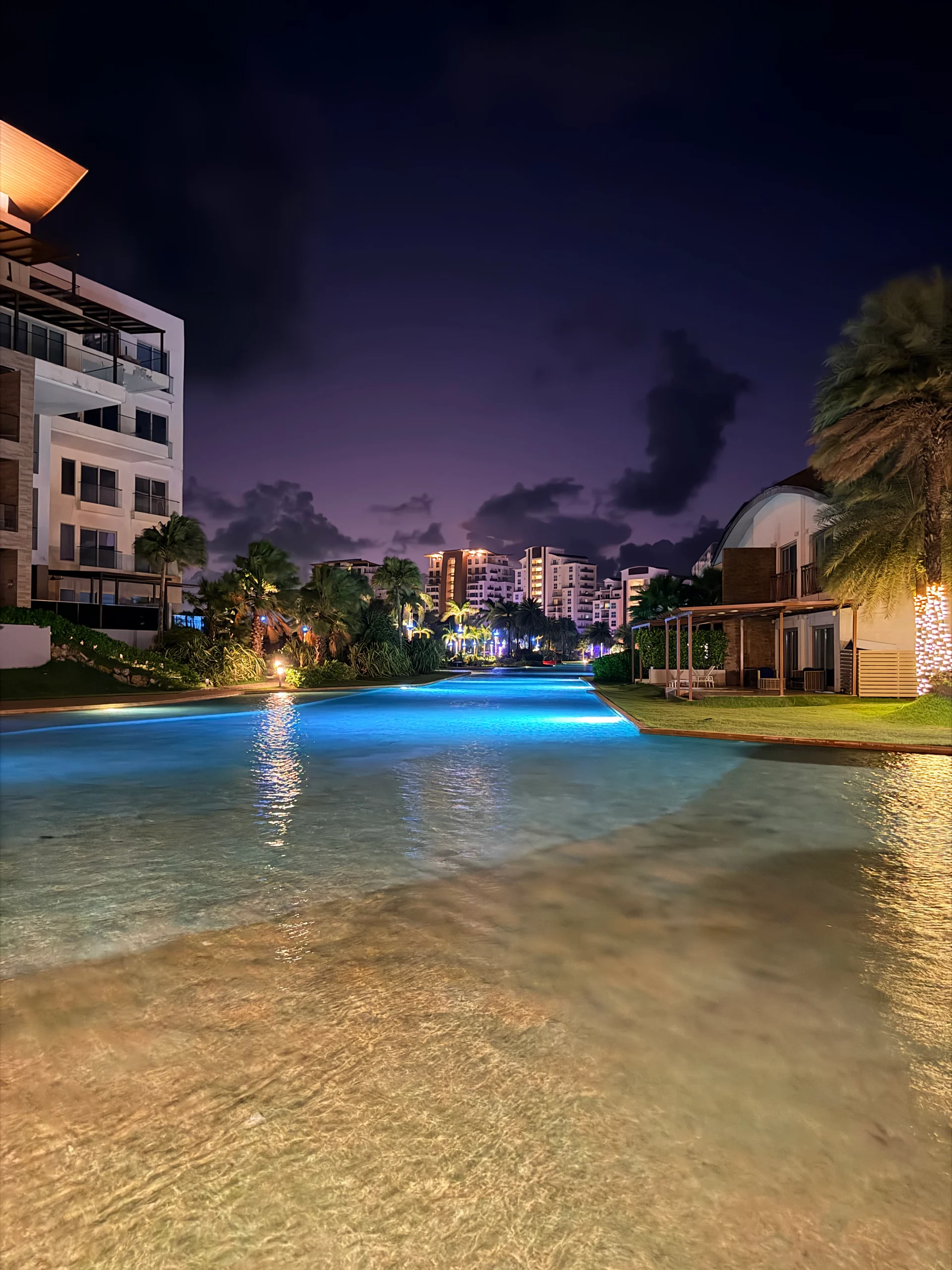 Vue nocturne sereine d'une piscine de luxe dans un complexe hôtelier à Playa Escondida, Panama. L'eau éclairée reflète les bâtiments environnants et la luxuriante végétation tropicale, créant une atmosphère paisible et invitante.