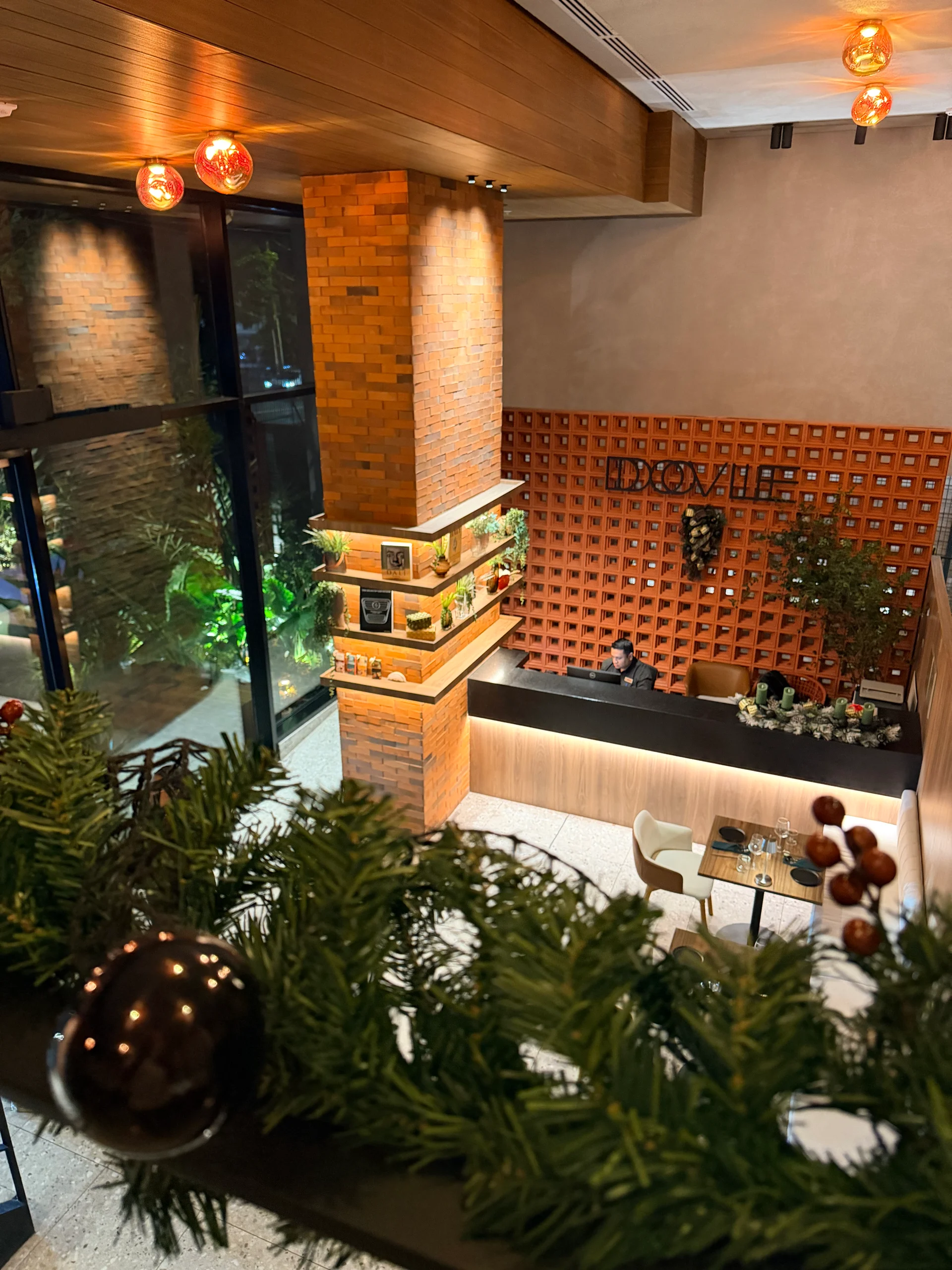 Elegant interior view of a restaurant lobby decorated for the holidays.  A modern reception desk with a textured brick wall backdrop and a geometric wooden screen creates a sophisticated atmosphere.