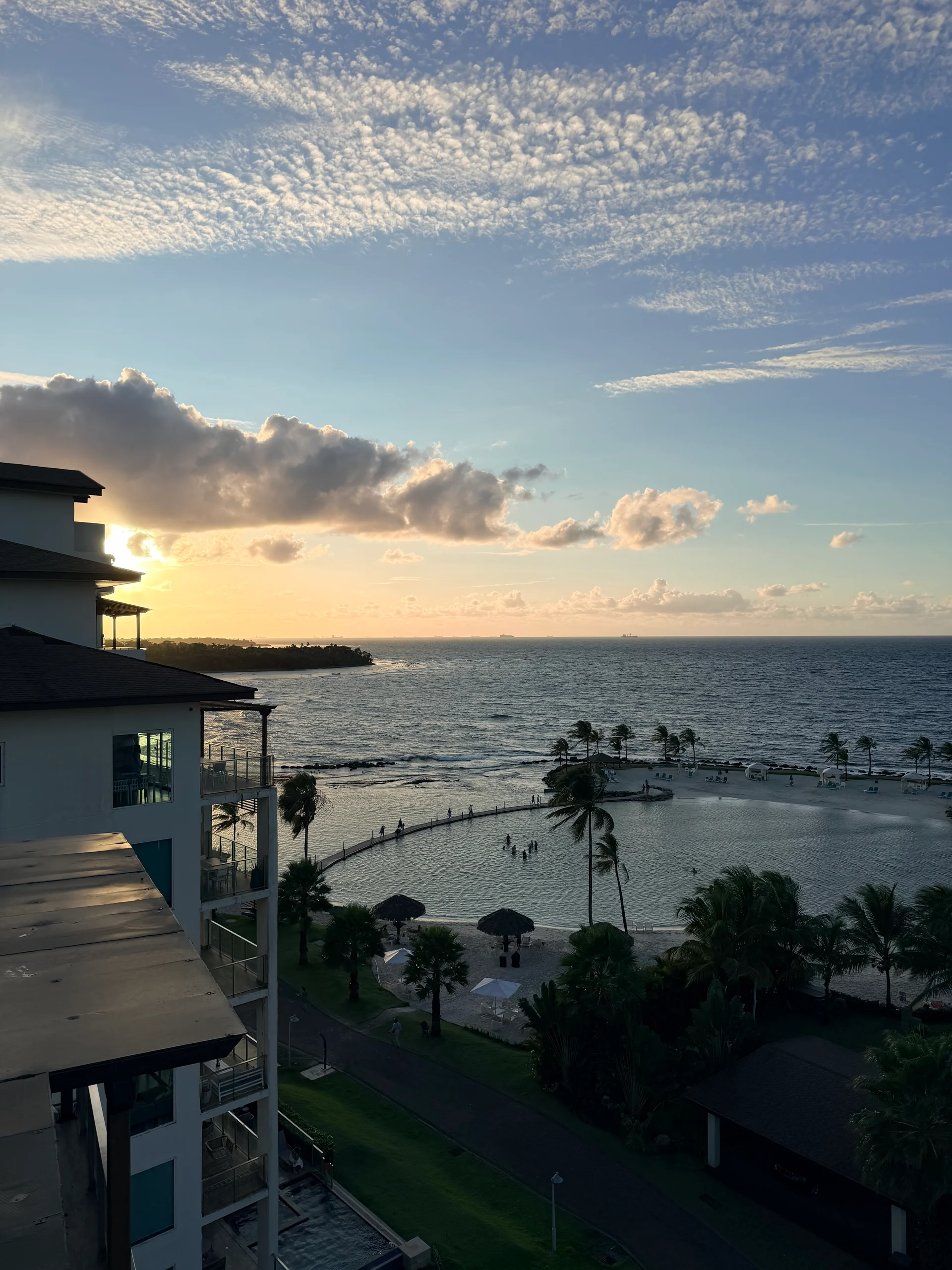 Une vue panoramique époustouflante de la piscine à débordement du Playa Escondida Resort surplombant la mer des Caraïbes turquoise au coucher du soleil. Des palmiers et une architecture moderne encadrent la scène, créant une évasion tropicale paisible et luxueuse.