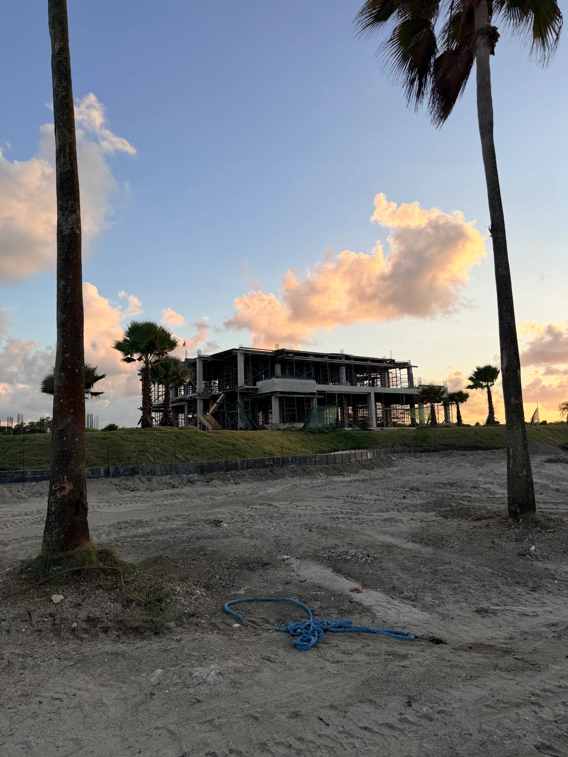 Construction d'un resort moderne en bord de mer à Playa Escondida, Colón, Panama, capturée lors d'un coucher de soleil vibrant. Des palmiers encadrent le bâtiment partiellement achevé, présentant une atmosphère luxueuse et tropicale.