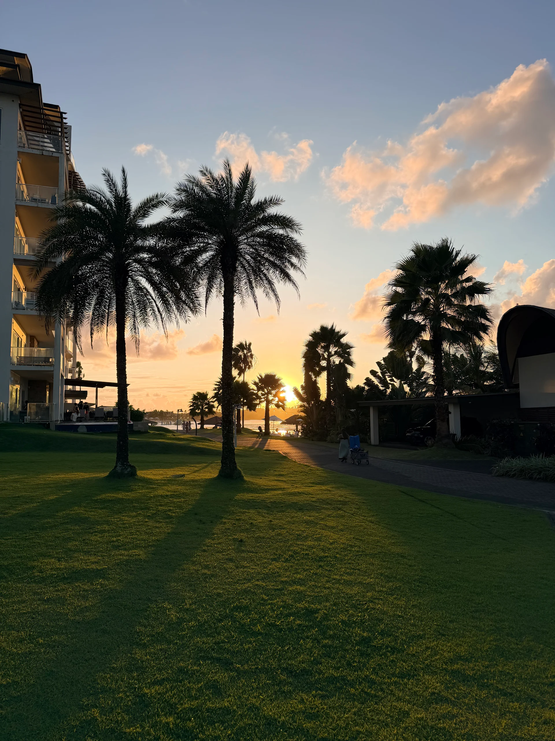 Une vue sereine du coucher de soleil au Playa Escondida Resort au Panama. De luxuriantes palmiers encadrent un coucher de soleil vibrant sur l'océan, avec un chemin menant à l'eau. Les clients se promènent le long du sentier, profitant de l'atmosphère paisible.