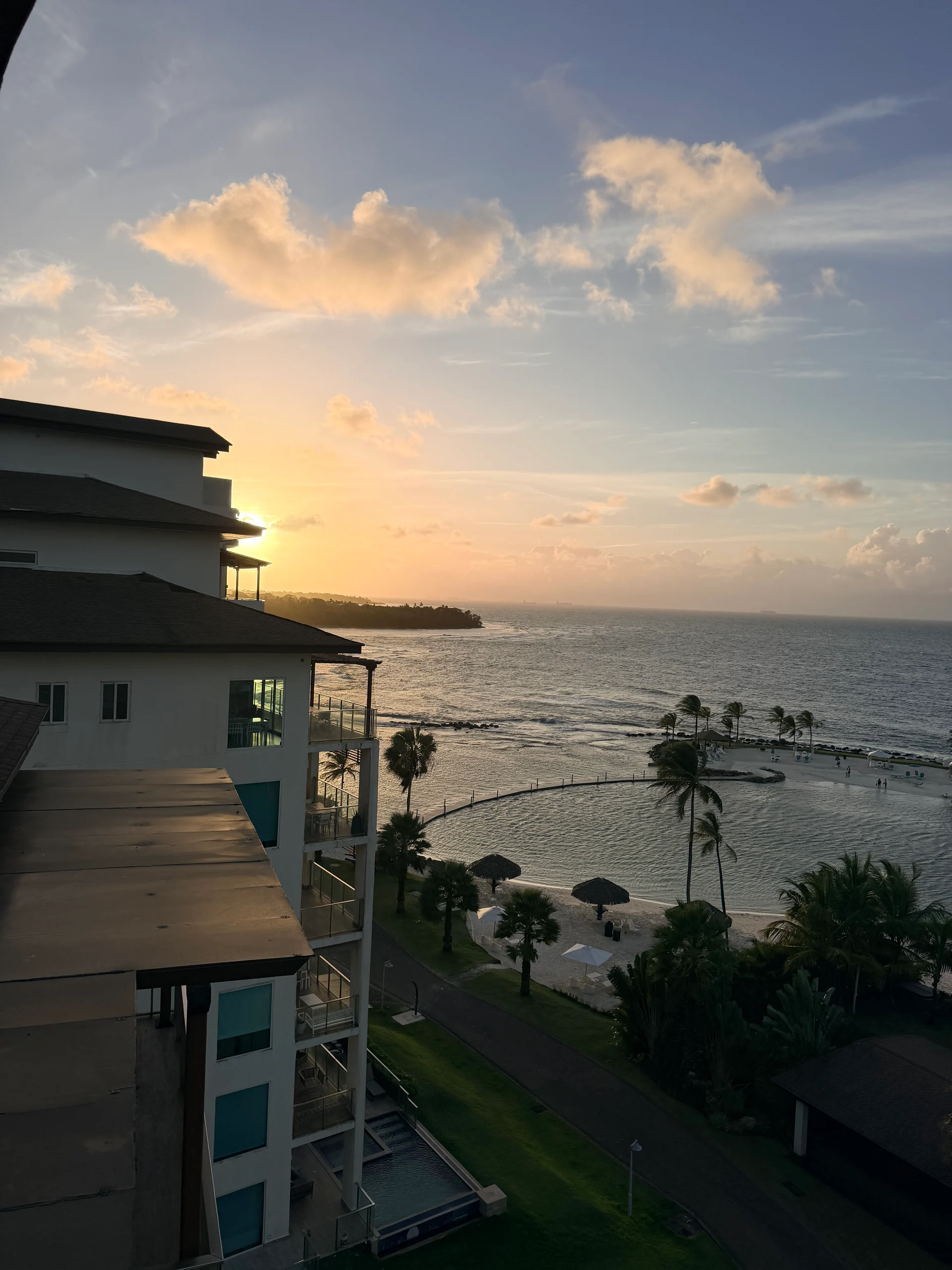 Une vue imprenable sur le coucher de soleil au-dessus d'une crique protégée à Playa Escondida Resort au Panama. L'image présente l'architecture moderne du complexe, les palmiers et une plage immaculée aux eaux calmes et turquoise. Des clients peuvent être vus profiter du coucher de soleil.